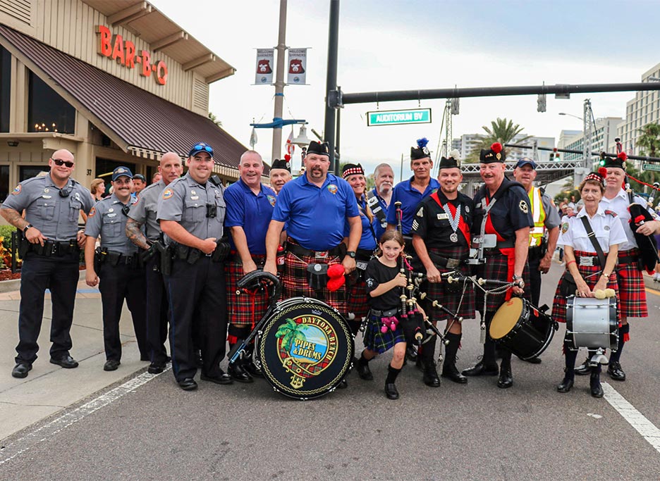 Shriners who are members of a pipes and drums unit, a patient, family, and law enforcement officers outside before parade