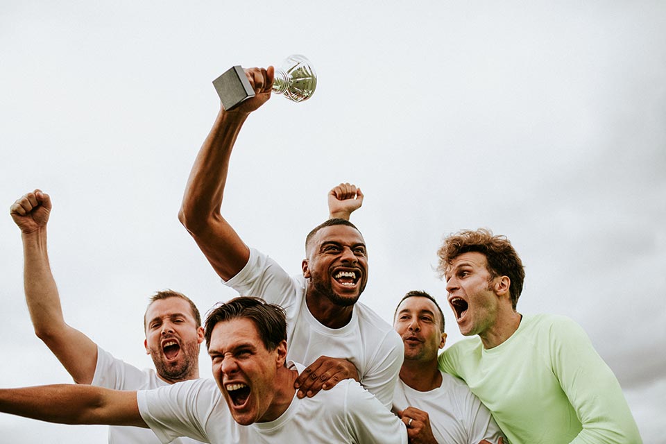 male teammates celebrating outside, holding trophy