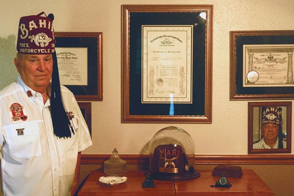 Bruce Carter de pie junto a una credenza y premios