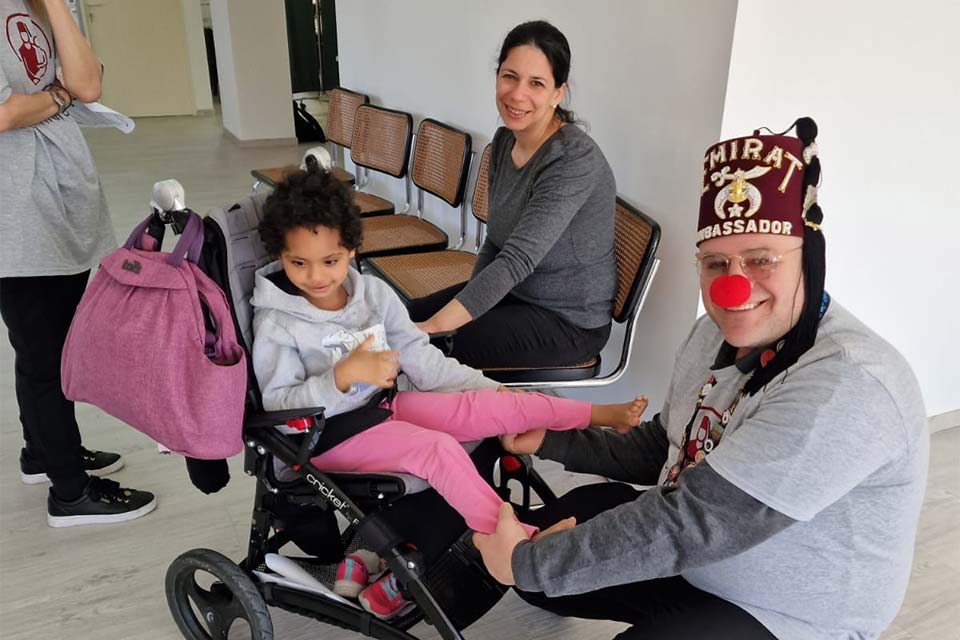 Paciente femenina en silla de ruedas con mamá y un payaso sentado junto a ella