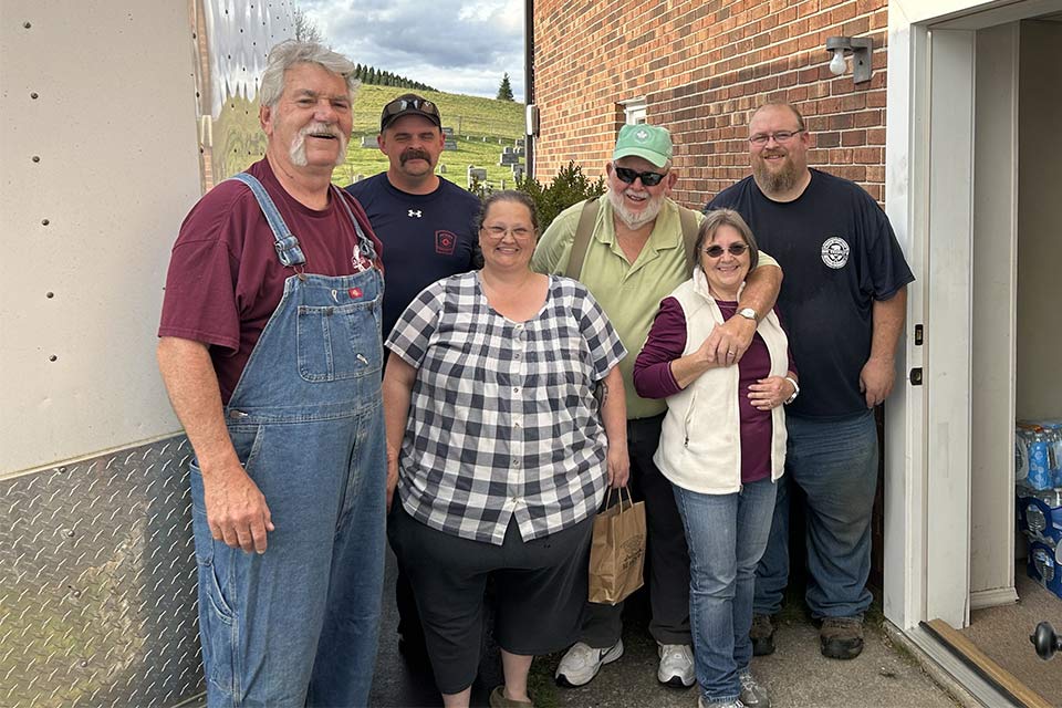 Six adults standing in a row next to a trailer and open door.
