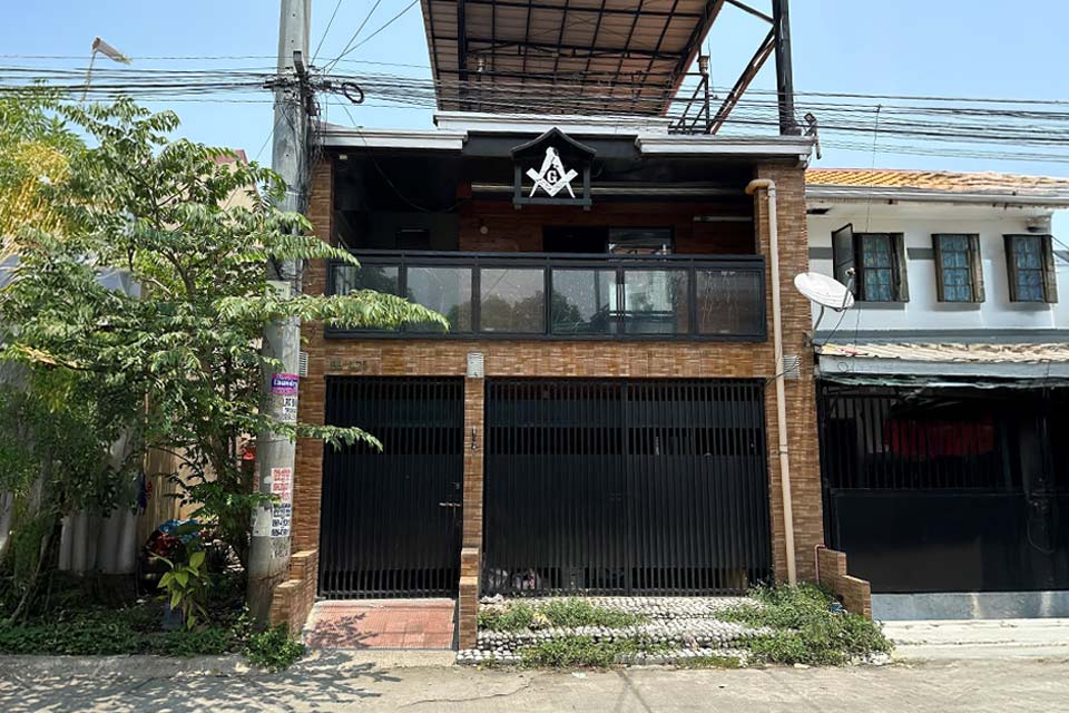 Una casa de dos pisos en una calle con un símbolo masónico colgando del balcón del segundo piso.