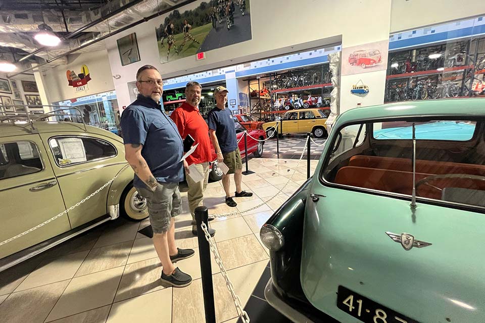 três homens em um museu de automóveis