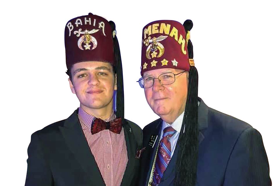Patient Ambassador Riley, wearing a fez, proudly standing next to his mentor, Imperial Sir Jim Cain, also wearing a fez