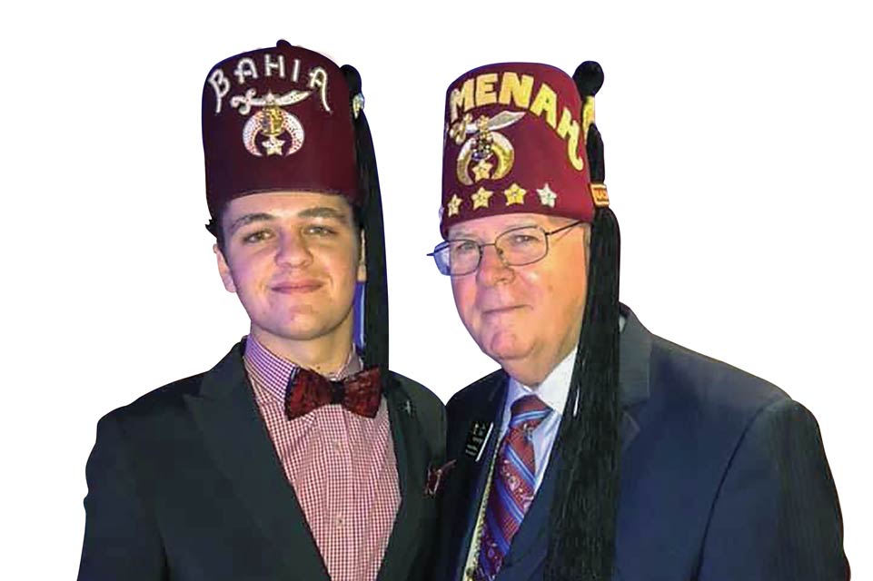 O paciente Embaixador Riley, usando um fez, orgulhosamente ao lado de seu mentor, Imperial Sir Jim Cain, também usando um fez