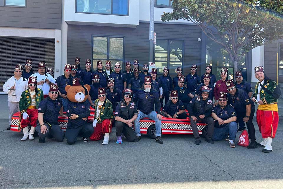 Clubes y unidades del Proyecto 3-5-7; logotipo de Shriners International; equipo de sección Asiya Shriners #357clubsunits; una foto grupal de Asiya Shriners frente a un edificio.