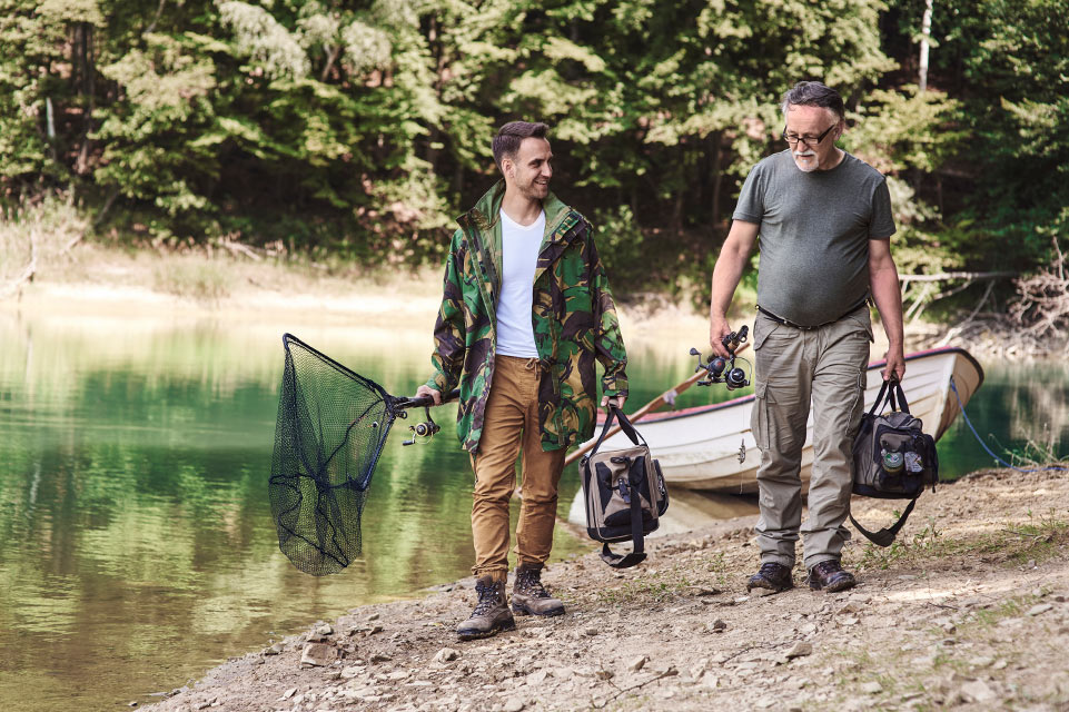 two men walking near lake with fishing gear